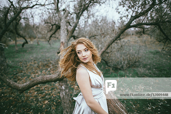 Glamouröse kaukasische Frau  die sich die Haare in der Nähe eines Baumes zuwirft