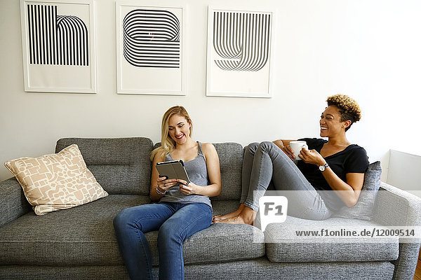 Frauen trinken Kaffee und benutzen ein digitales Tablet auf dem Sofa