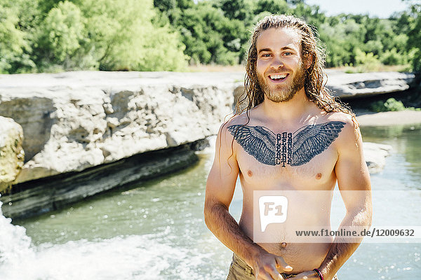 Lächelnder kaukasischer Mann mit Brusttattoo in der Nähe eines Flusses
