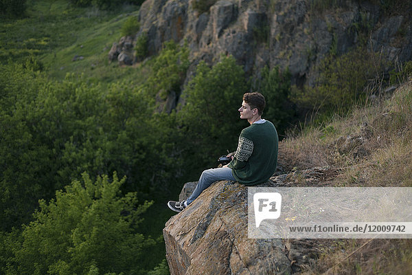 Kaukasischer Mann sitzt auf einem Felsen und bewundert die Landschaft