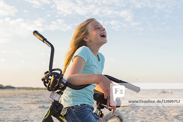 Laughing Caucasian girl leaning on bicycle at beach