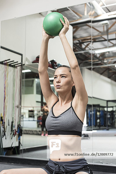 Mixed race woman lifting heavy ball in gymnasium