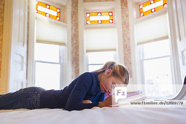 Caucasian girl laying on bed writing in notebook