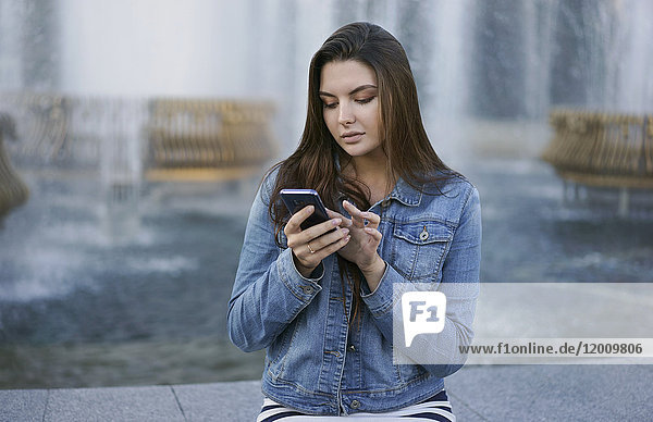 Kaukasische Frau  die am Brunnen eine SMS auf ihrem Handy schreibt