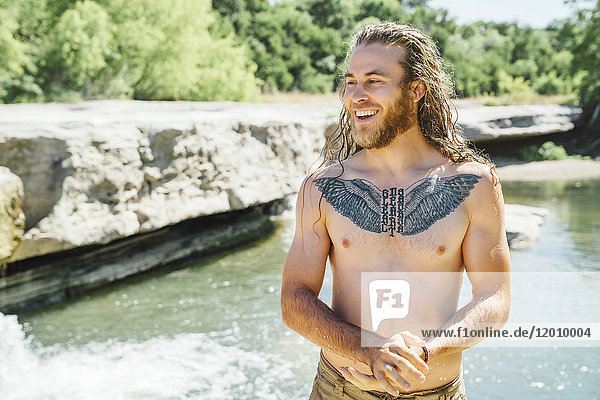 Lächelnder kaukasischer Mann mit Brusttattoo in der Nähe eines Flusses