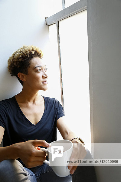 Gemischtrassige Frau trinkt Kaffee auf der Fensterbank