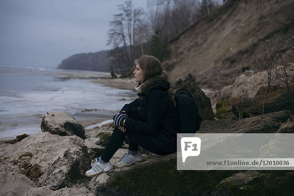 Kaukasische Frau sitzt auf Felsen in der Nähe des Meeres