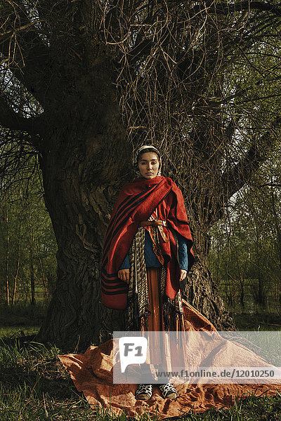 Kaukasische Frau in traditioneller Kleidung steht neben einem Baum