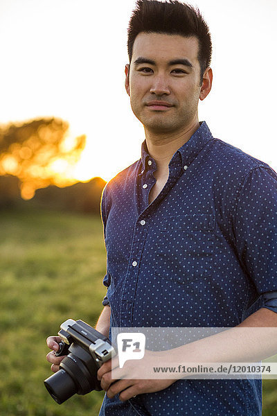 Lächelnder chinesischer Mann mit Kamera in einem Feld