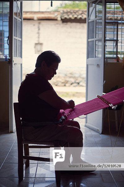 Hispanic woman weaving fabric on loom near doorway