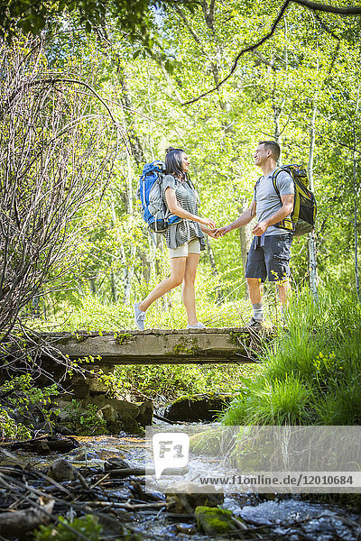 Couple carrying backpacks across bridge in woods