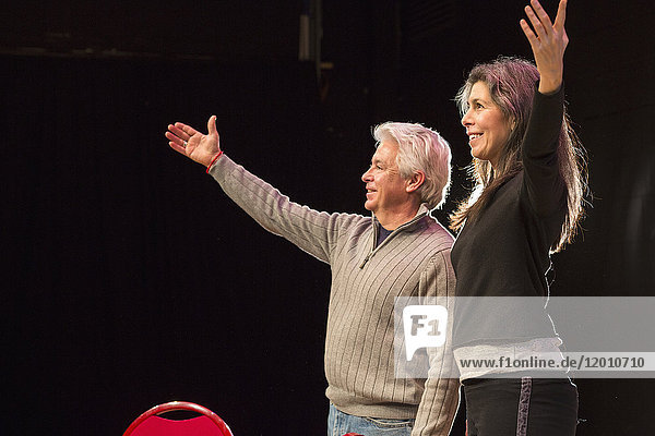 Hispanischer Mann und Frau mit erhobenen Armen auf einer Theaterbühne