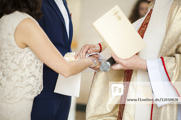 Priester und Paar reichen sich bei der Hochzeit die Hände