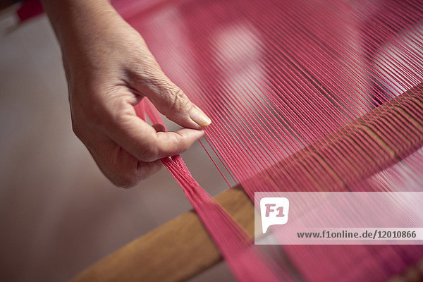 Hand of Hispanic woman weaving fabric on loom