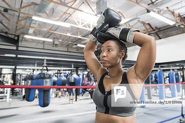 Black woman resting with arms raised in boxing ring