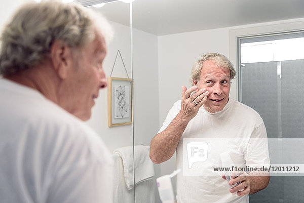 Caucasian man applying lotion to face in mirror