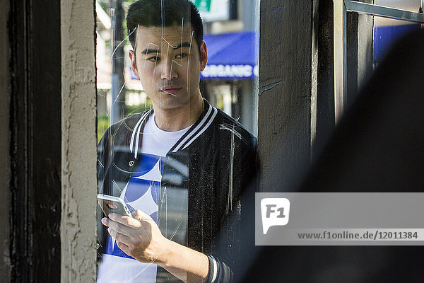 Seriöser chinesischer Mann  der hinter dem Fenster eine SMS mit seinem Handy schreibt