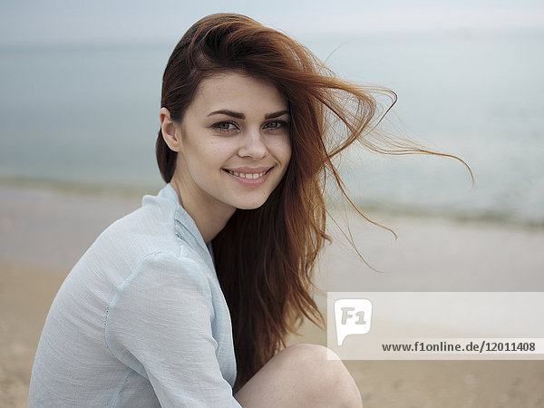 Wind weht Haare der kaukasischen Frau sitzen am Strand