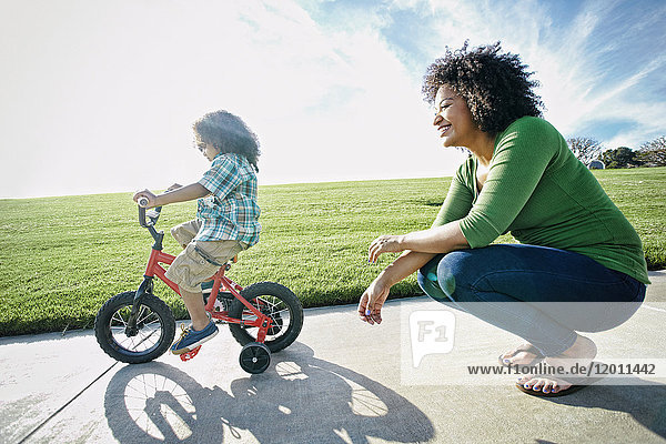 Gemischtrassige Mutter beobachtet Sohn beim Fahrradfahren