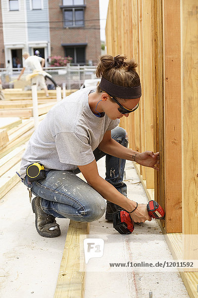 Caucasian woman drilling lumber at construction site