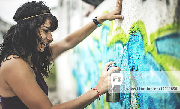 Eine junge Frau sprüht Graffiti auf eine Wand.