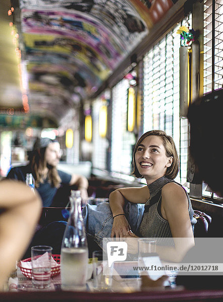 Lächelnde Frau sitzt in einer Kabine in einem Diner  schaut auf und unterhält sich mit Freunden.