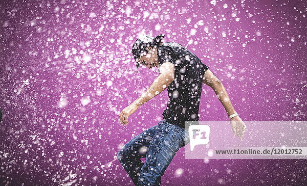 Young man standing in a shower of water drops.