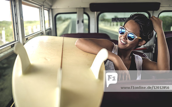 Junge Frau  die mit einem Surfbrett in einem Bus sitzt.
