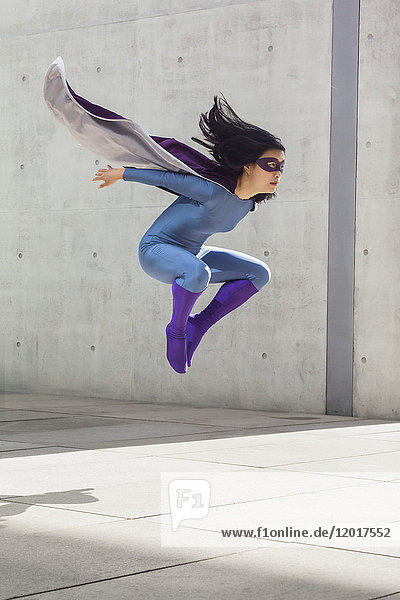 Weibliche Superheldin schwebt in der Luft gegen die Wand.