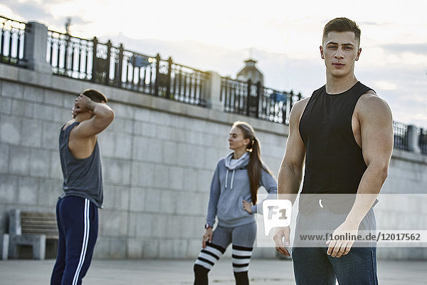 Porträt eines selbstbewussten jungen Athleten  der mit Freunden gegen die Brücke steht.