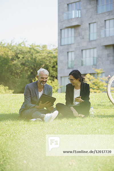 Smiling business coworkers looking at folder while sitting on grassy field
