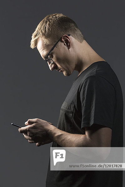 Seitenansicht des Mannes mit dem Handy im Stehen vor grauem Hintergrund