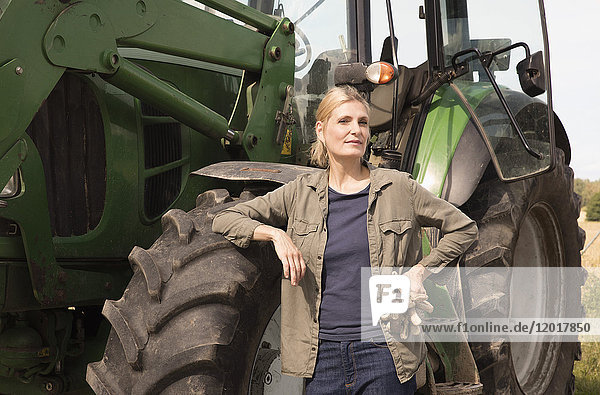 Portrait einer reifen Frau  die an einem sonnigen Tag am Traktor steht.