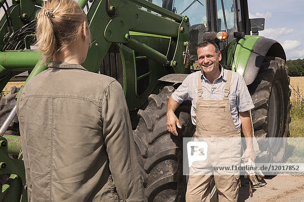 Männlicher Bauer im Gespräch mit einer Frau  während er an einem sonnigen Tag an einer Landmaschine steht.