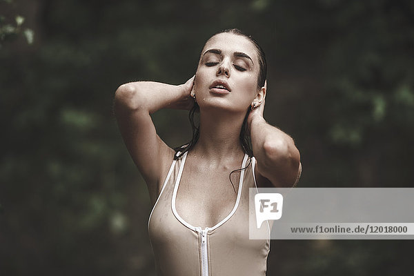 Sinnliche junge Frau mit Händen hinter dem Kopf in Badebekleidung im Wald