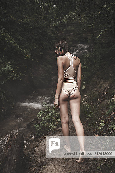 Rückansicht einer Frau in Badebekleidung  die auf dem Weg durch den Wald läuft.
