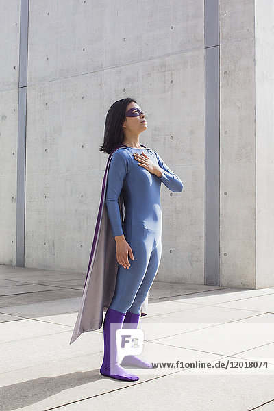 Confident woman wearing superhero costume standing on floor by wall