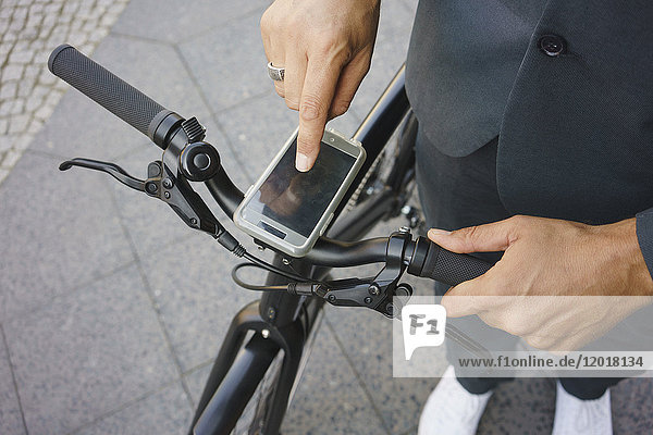 Niedriger Teil des Geschäftsmannes  der das Smartphone am Fahrradgriff benutzt  während er auf der Straße steht.