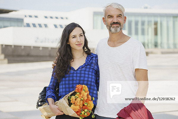 Confident couple with bouquet standing in city on sunny day