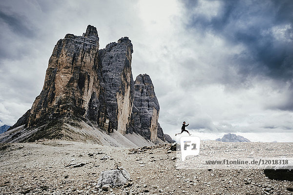 Low angle view of teenage boy jumping over rocks in alps against cloudy sky  South Tyrol  Italy