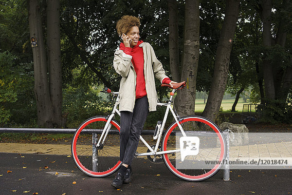 Mittlere erwachsene Frau beim Telefonieren mit dem Fahrrad im Park