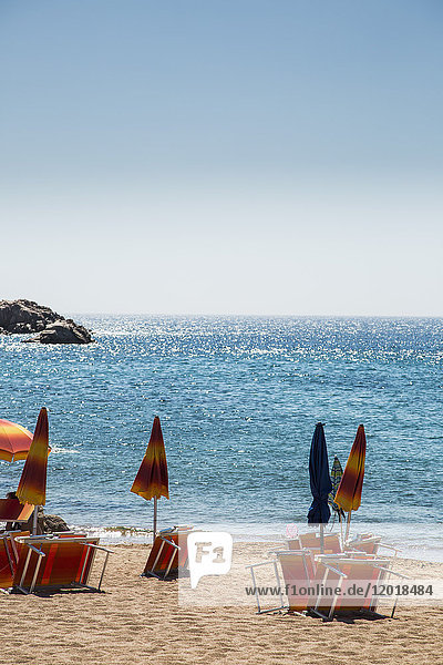 Geschlossene Sonnenschirme mit Liegestühlen am Strand gegen klaren blauen Himmel an sonnigen Tagen