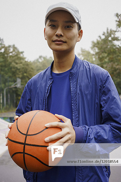 Porträt eines jungen Mannes  der den Ball hält  während er im Park steht.