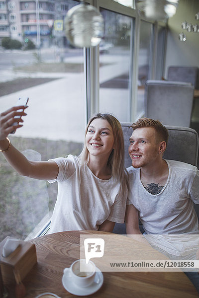 Hochwinkelansicht eines jungen Paares  das im Restaurant sitzt und sich selbst mit dem Handy fotografiert.