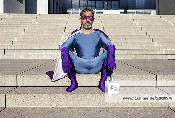 Porträt eines als Superhelden verkleideten Mannes auf einer Treppe sitzend