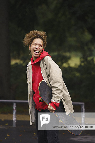 Fröhliche Frau mit Skateboard beim Stehen im Park
