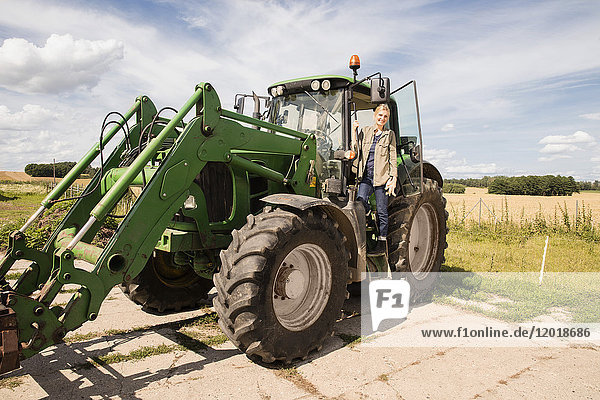 Full length of smiling mature woman standing on agricultural machinery against sky