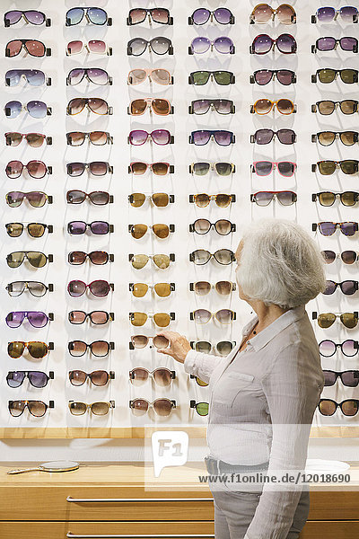 Seitenansicht der Seniorin bei der Wahl der Sonnenbrille im Geschäft