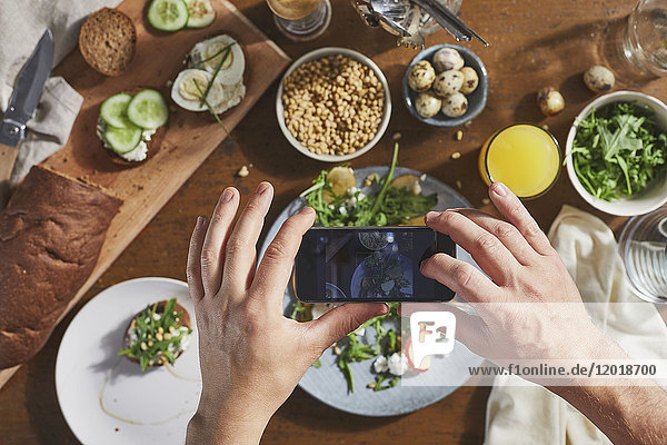 Beschnittenes Bild eines Mannes  der Essen auf dem Tisch mit dem Handy fotografiert.