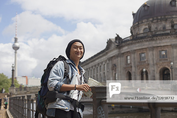 Smiling young male tourist standing with map by railing against Bode Museum  Berlin  Germany